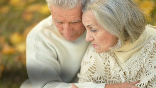 an elderly couple hugging and looking sad